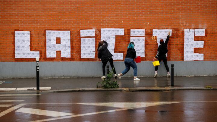 Three feminist activists placard posters of a drawing by French cartoonist Charb to read " Laicite " in Montreuil, on October 20, 2020.