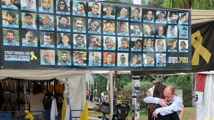 People embrace in front of a banner displaying photos of hostages at the ‘hostage square’.