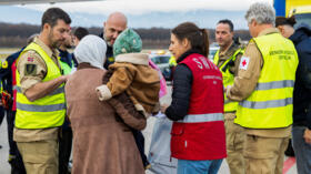 A woman from Gaza carries her baby after landing at Geneva Airport in Switzerland, where they will receive medical treatment, on November 28, 2025