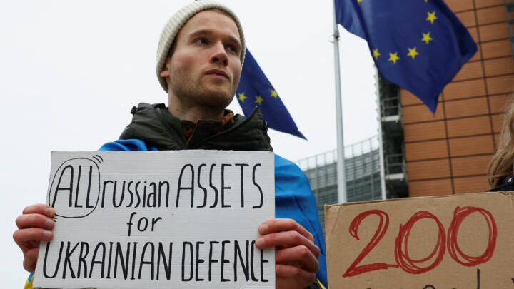 A man holds a banner as people demonstrate outside the European Commission, in support of using frozen Russian assets to finance Ukraine, in Brussels, Belgium, December 17, 2025.