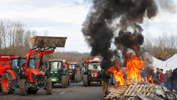French farmers gather around a fire as they block the highway near Urt, southwestern France, to protest against a mass cull of cows ordered to contain the spread of a skin disease.